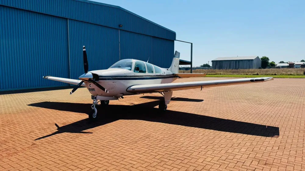 A front view of a white and dark grey single-engine propeller aircraft parked in front of a blue hangar.