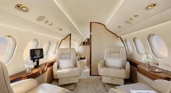 A luxurious aircraft cabin with cream leather seats, wood paneling, and large windows.
