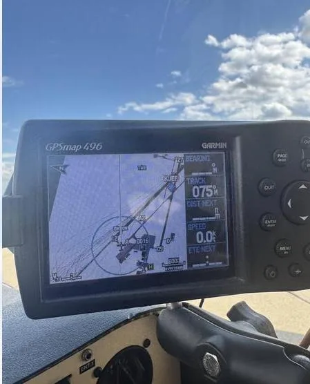 A Garmin GPSmap 496 portable GPS unit mounted in an aircraft, displaying navigation information against a cloudy sky.