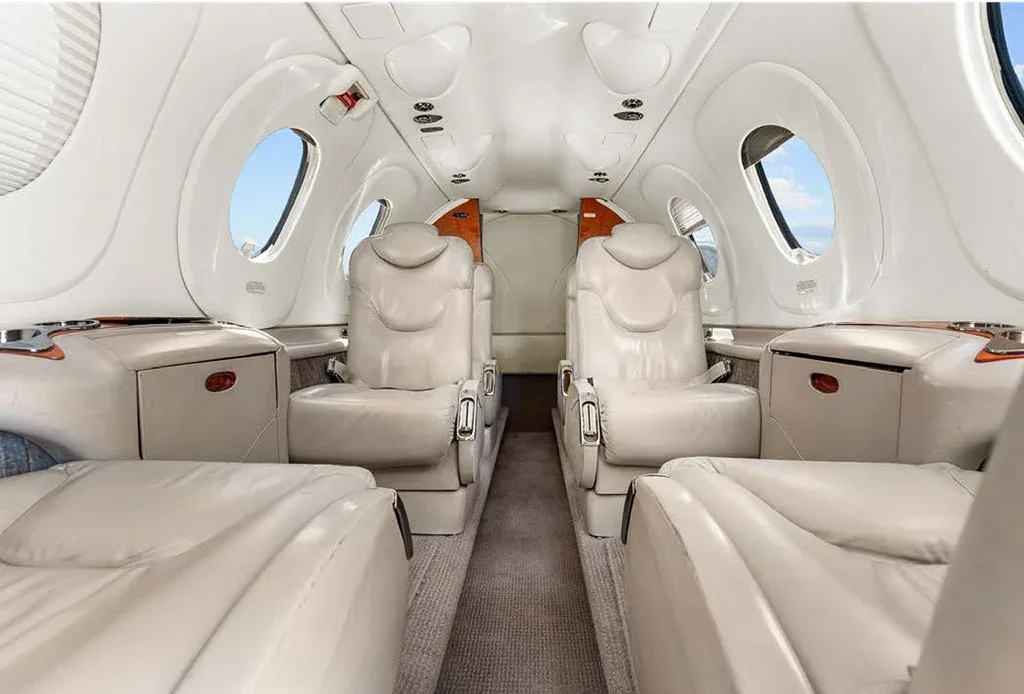 The luxurious beige leather interior cabin of a private jet, featuring club seating and large windows.