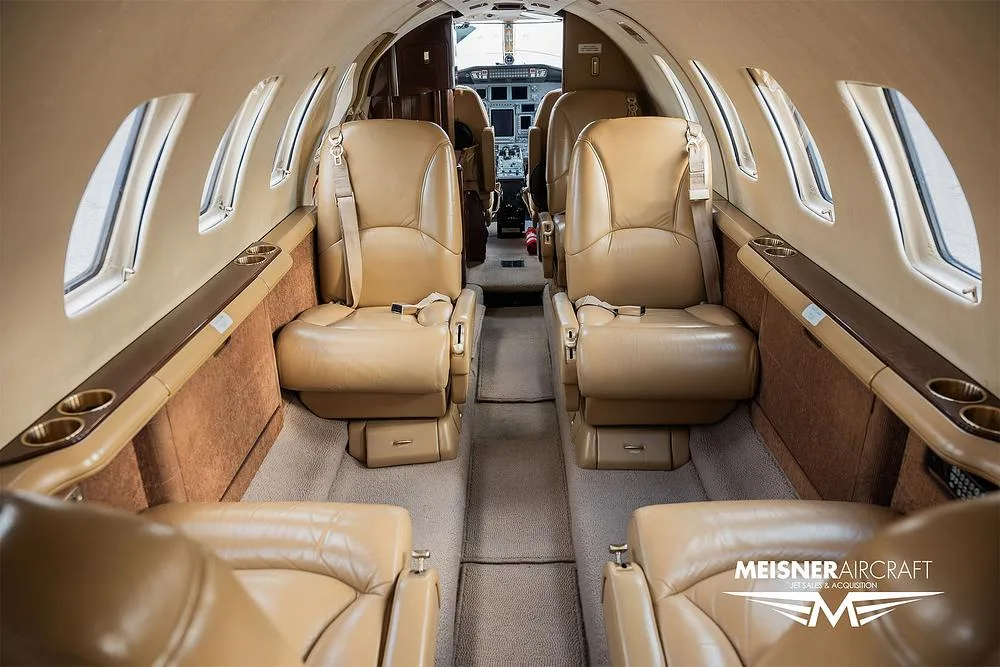 The interior cabin of a private jet featuring tan leather seats and a view towards the cockpit.