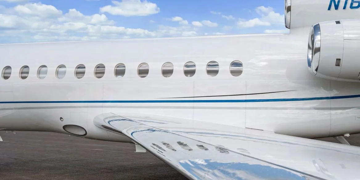A close-up view of the fuselage, windows, and wing of a white business jet with blue accent stripes.