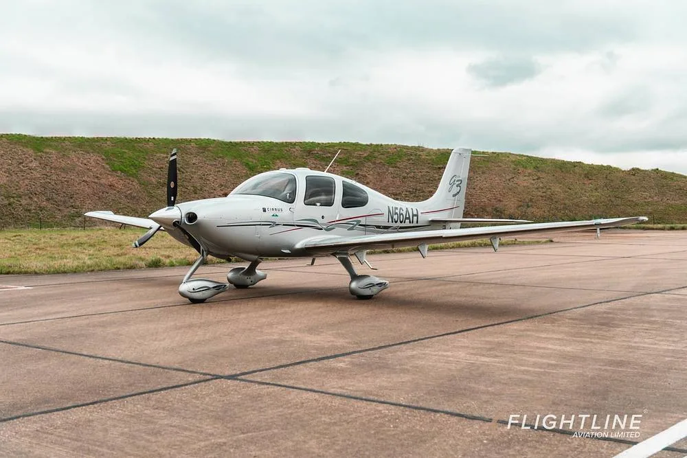 A front three-quarter view of the white Cirrus SR22 aircraft N56AH parked on a tarmac.