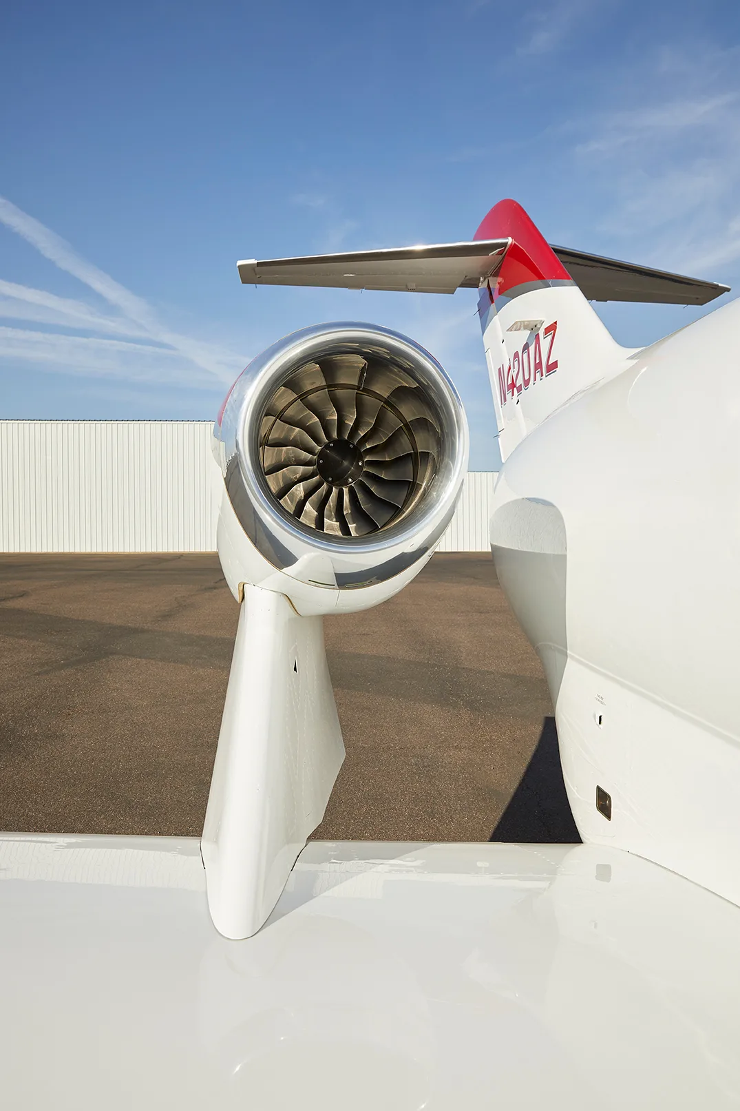 A close-up view of the over-wing engine and tail section, showing registration N420AZ, of a red and white HondaJet HA-420.