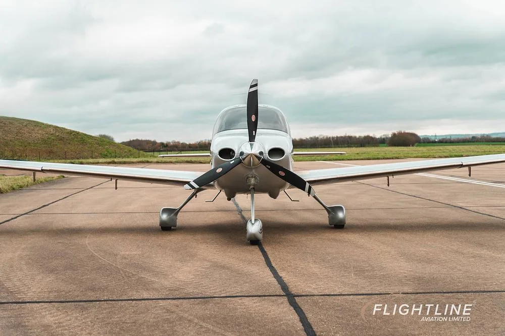 A head-on view of the white Cirrus SR22 aircraft N56AH with its propeller centered on a tarmac.