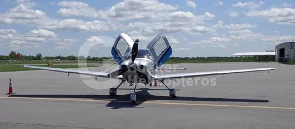 A silver Cirrus SR22 aircraft with its gull-wing doors open, viewed from the front on an airport tarmac.