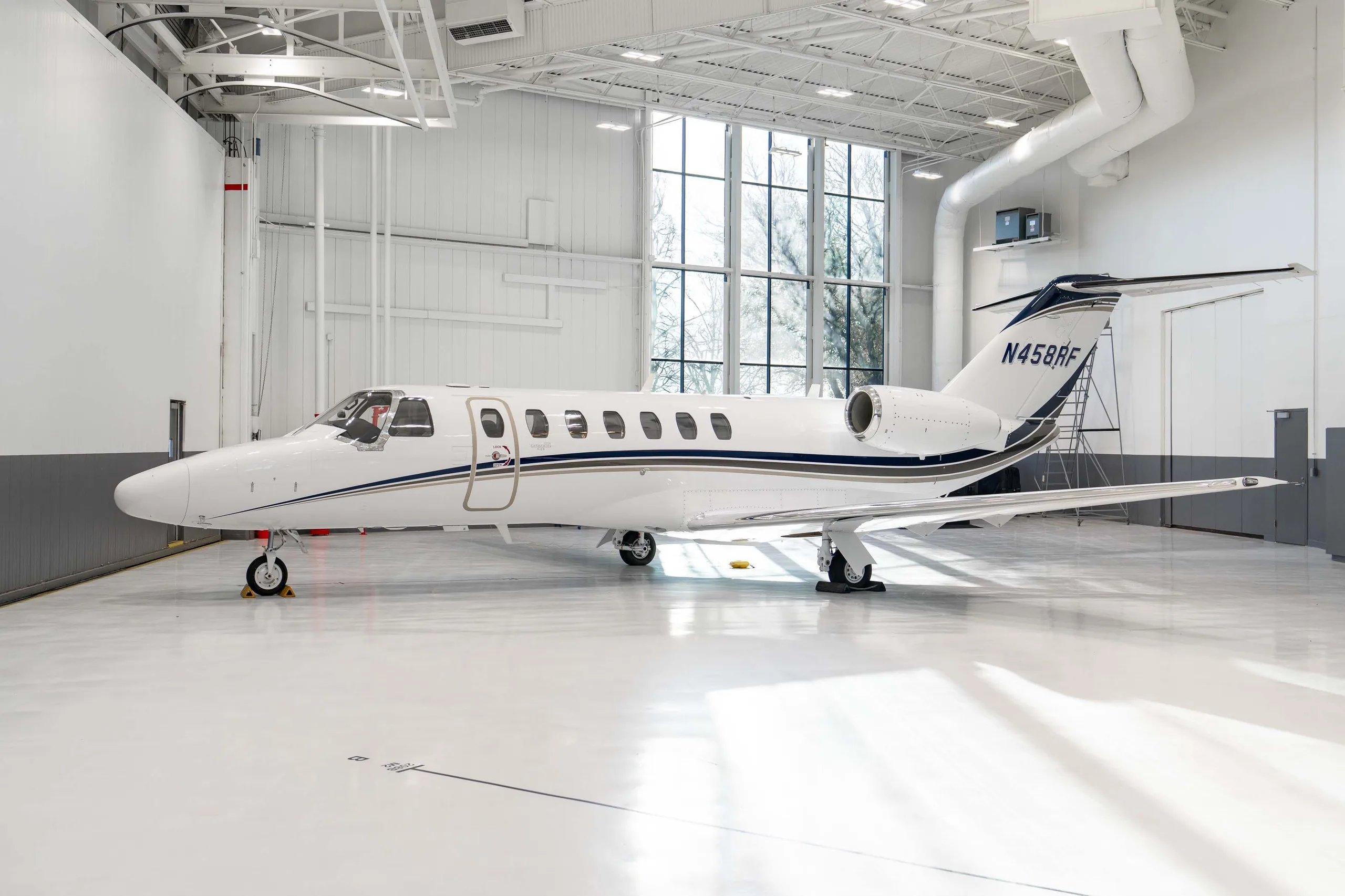 A white Cessna Citation CJ3 Gen2 business jet with blue and grey stripes, registration N458RF, parked inside a bright hangar.