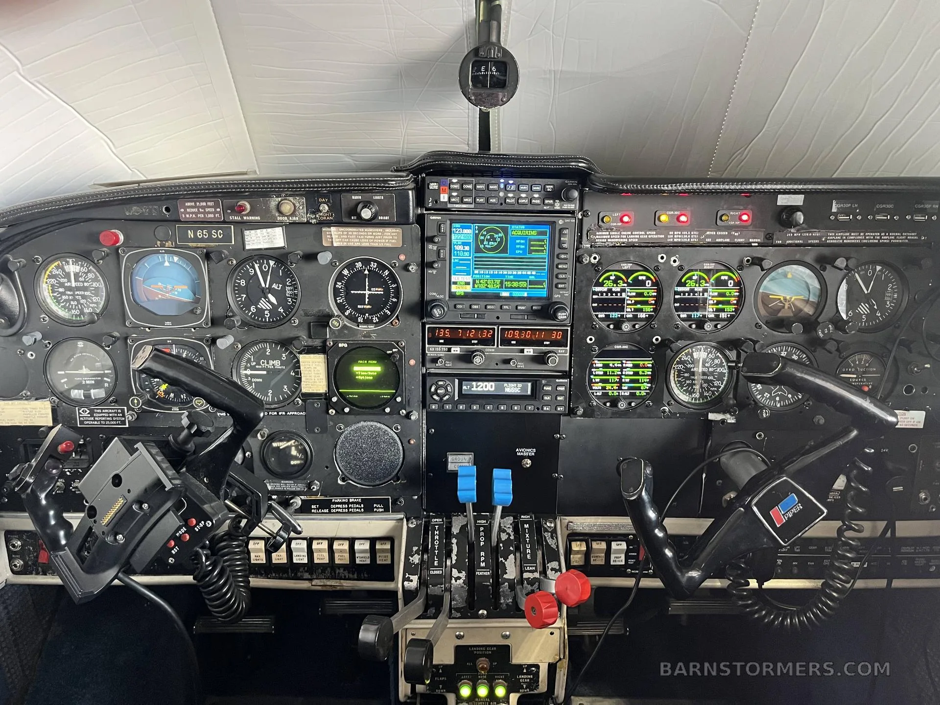 The cockpit of an aircraft, showing the instrument panel with analog gauges, digital displays, and control yokes.