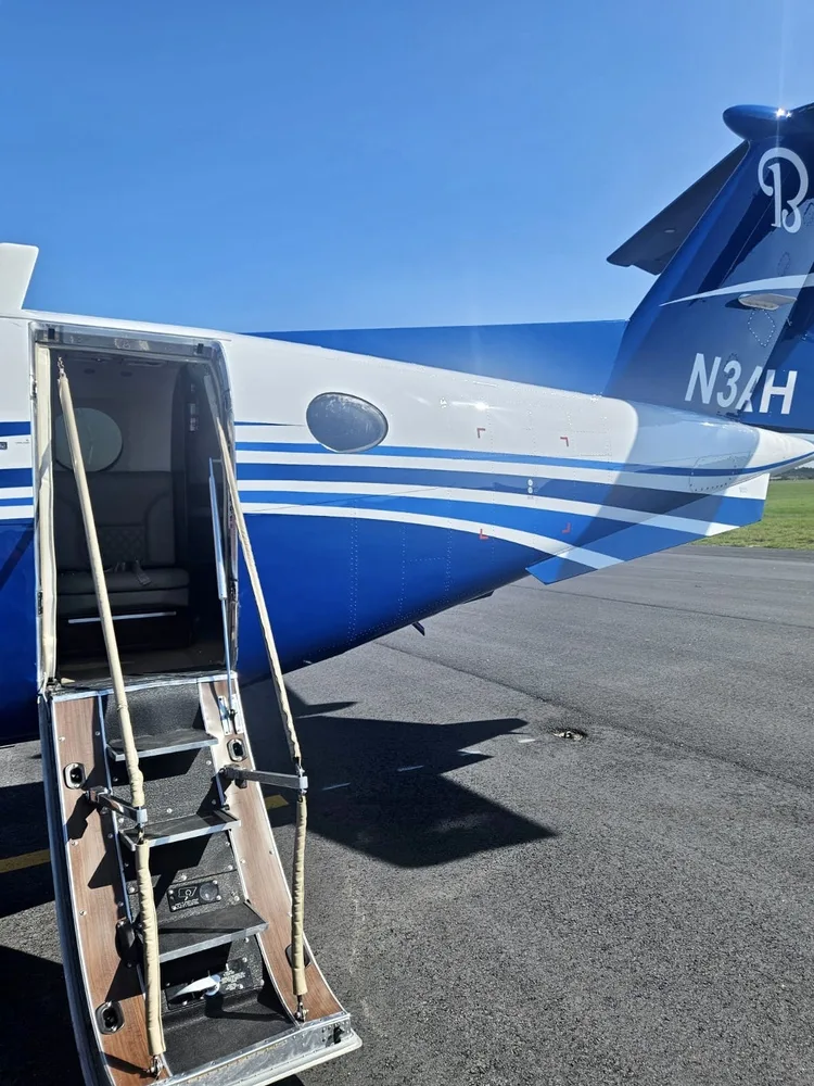 The rear fuselage of a white and blue Beechcraft King Air 350i aircraft with its airstair door open.