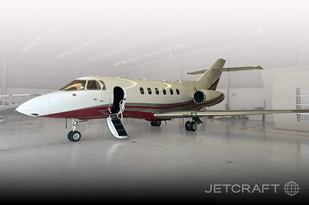 A white and red Hawker business jet with its door open and stairs extended, parked inside a hangar.
