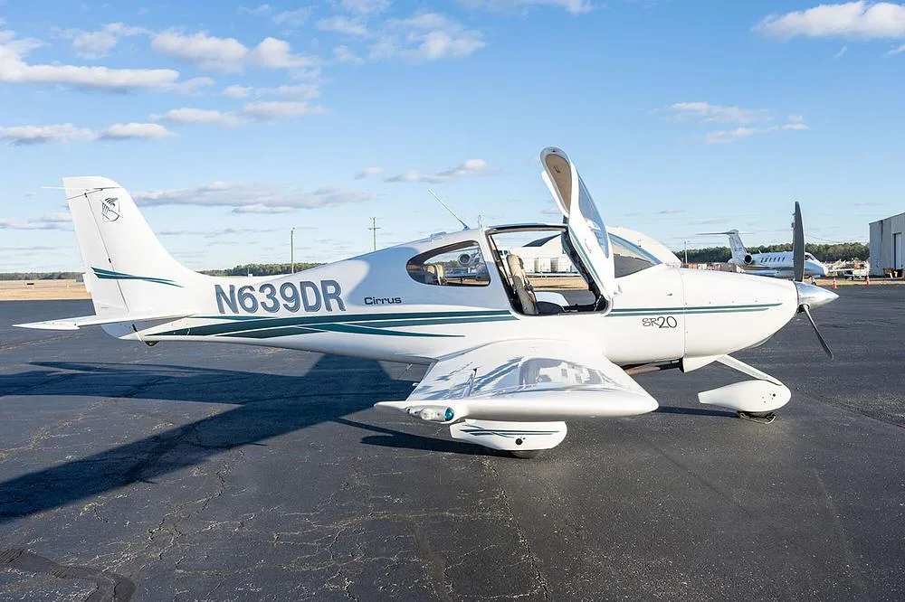A white Cirrus SR20 aircraft with green and grey stripes, registration N639DR, parked on an asphalt tarmac with one gull-wing door open.