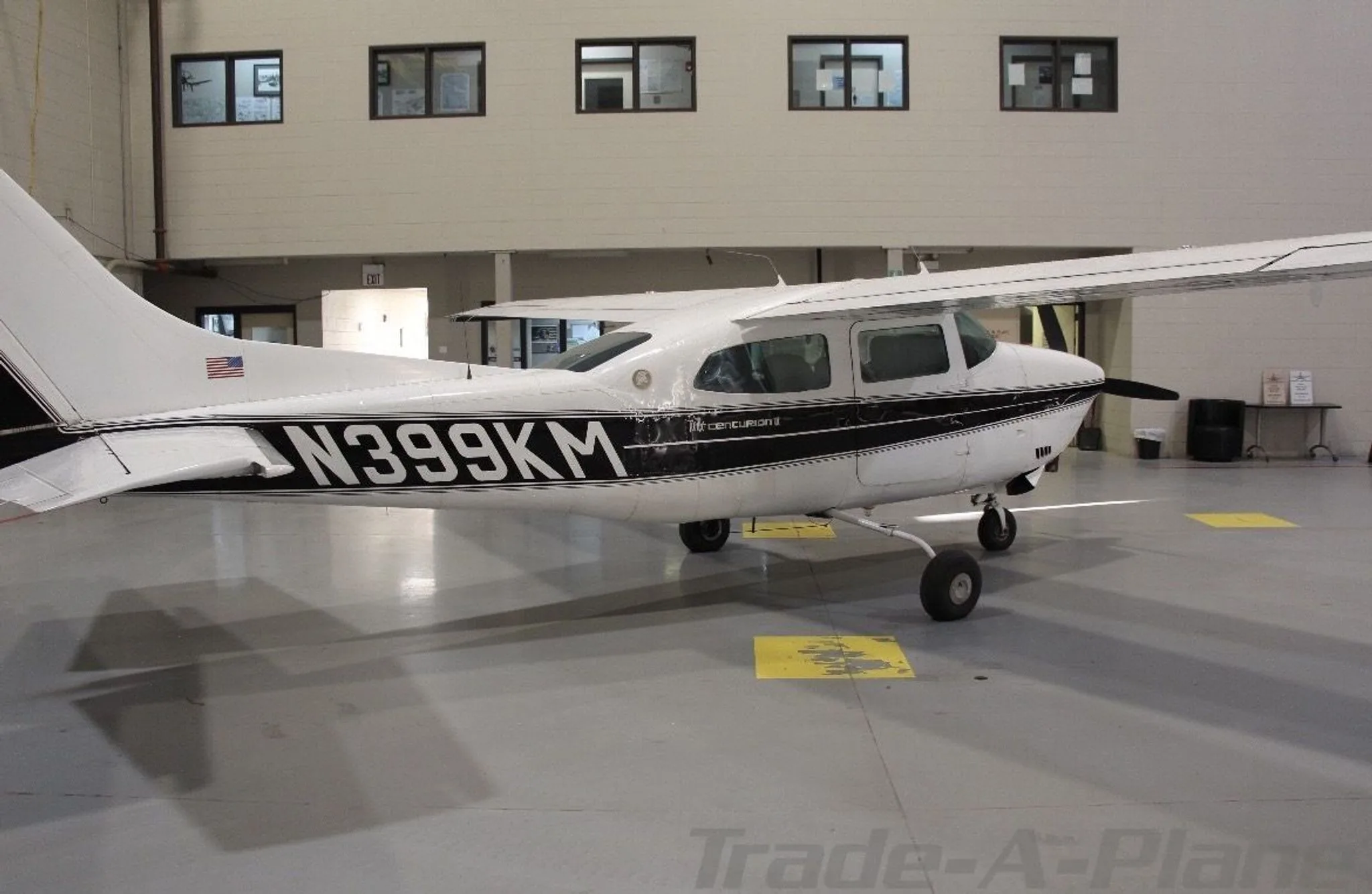 A white Cessna 210 Centurion with black stripes, seen from the rear-left in a hangar.