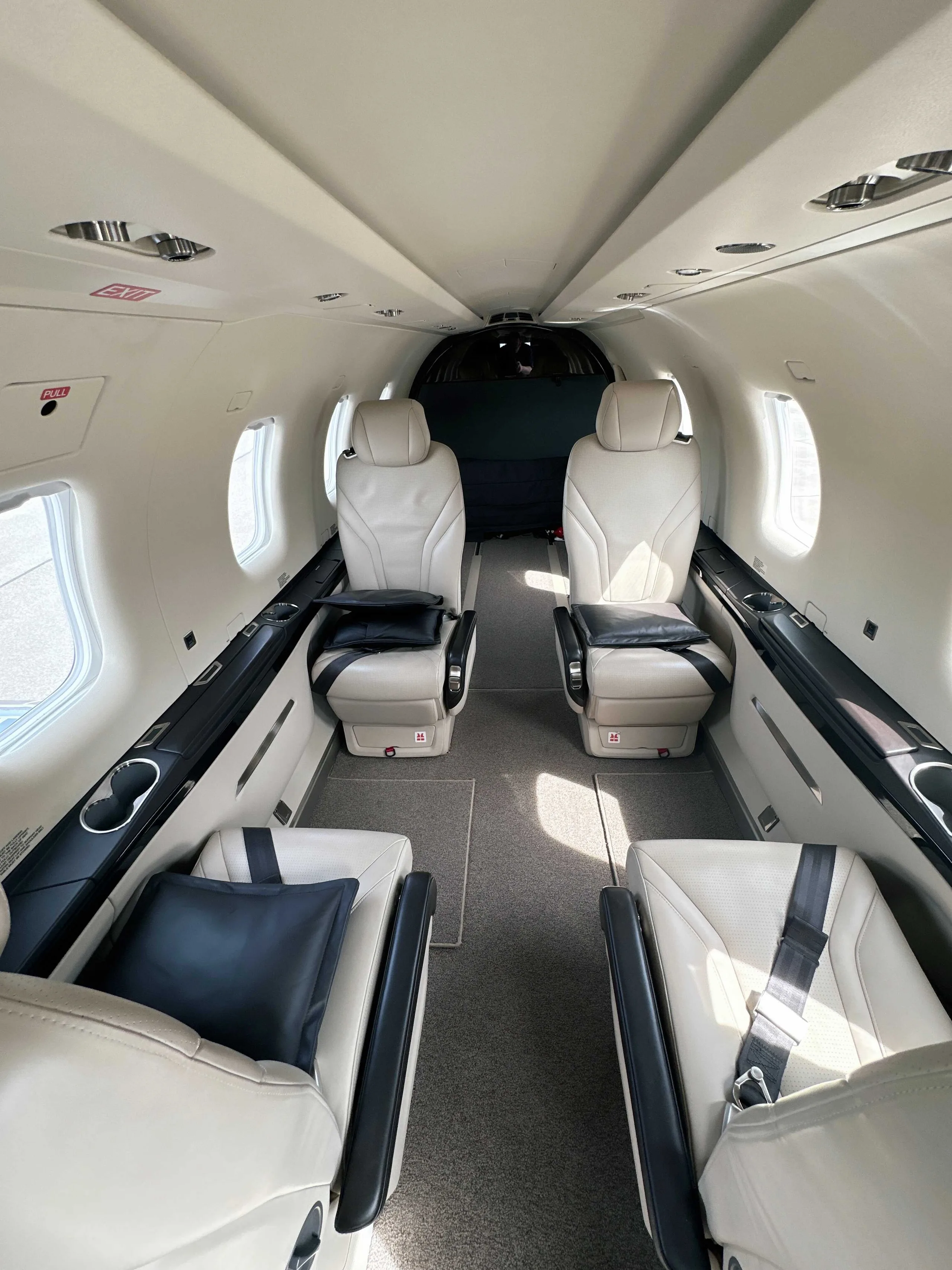 The interior cabin of an aircraft with four light-colored leather seats and dark pillows, facing forward.