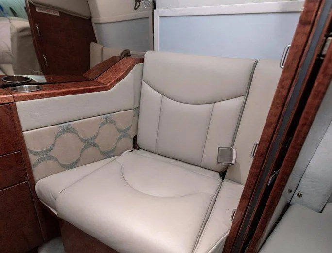 A close-up view of a beige leather seat and wood-paneled side console in a private jet cabin.