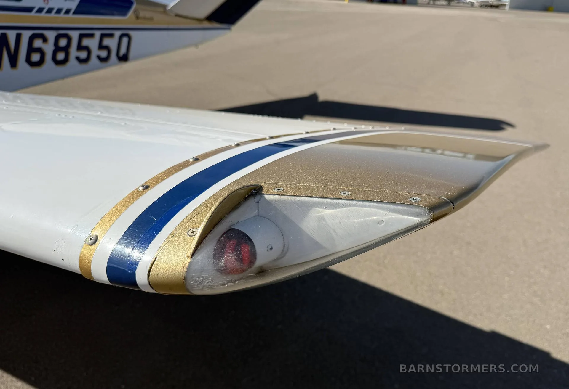 A close-up of the wingtip of the Beechcraft Bonanza, showing the navigation light and blue and gold stripe.