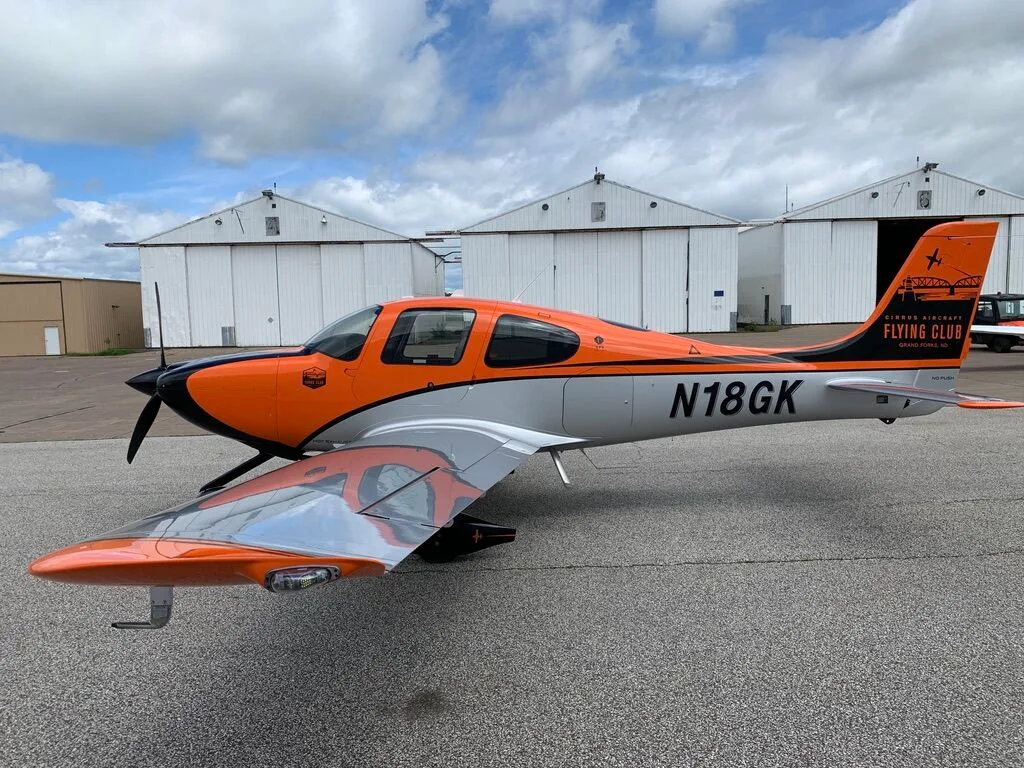 Side view of a Cirrus SR20 aircraft with orange, black, and silver paint scheme, showing the N18GK registration.