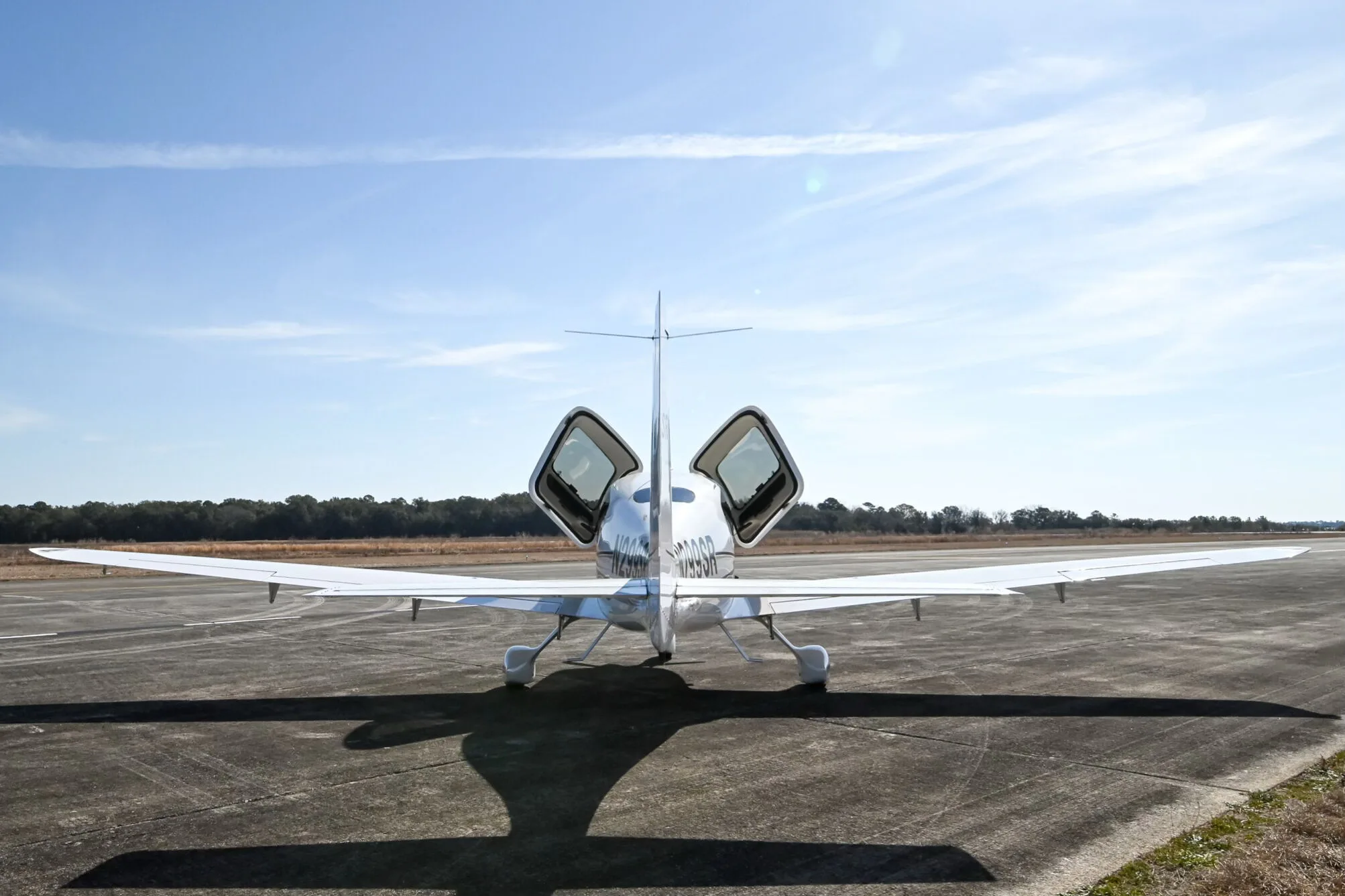 Rear view of a white Cirrus SR20 aircraft with its doors open, parked on an airfield.