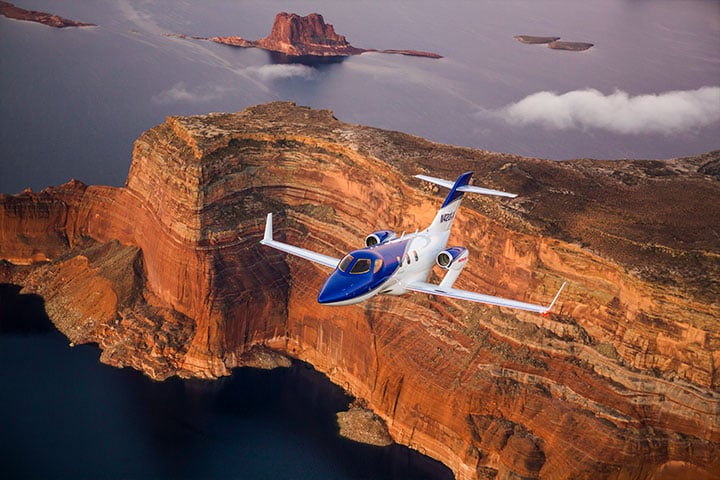 A HondaJet flying over a canyon and lake.