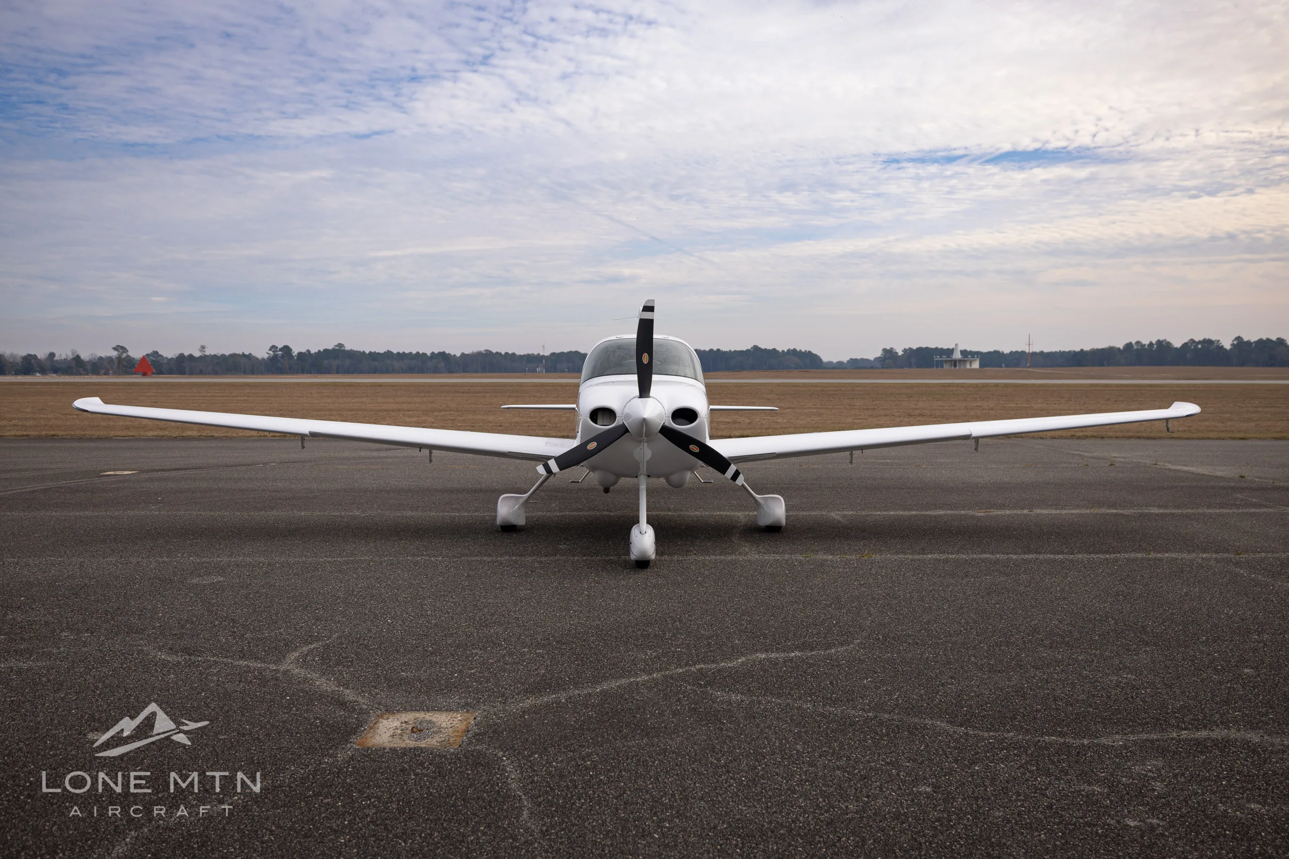 A white Cirrus SR20 aircraft with black and grey stripes, registration N898TX, viewed head-on from the front on an asphalt runway.