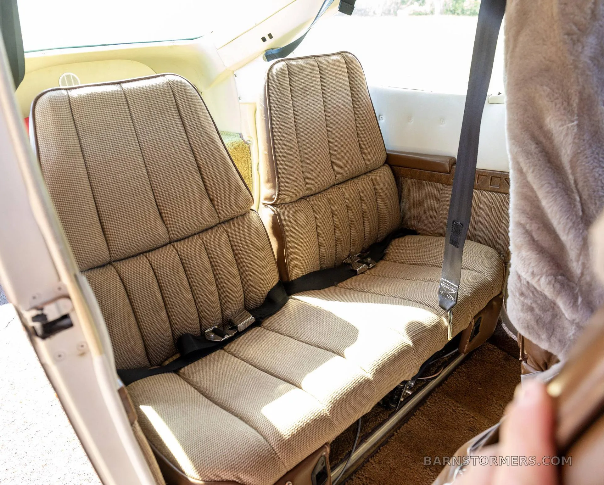 The rear cabin of the aircraft shows two tan patterned fabric seats with black seatbelts.