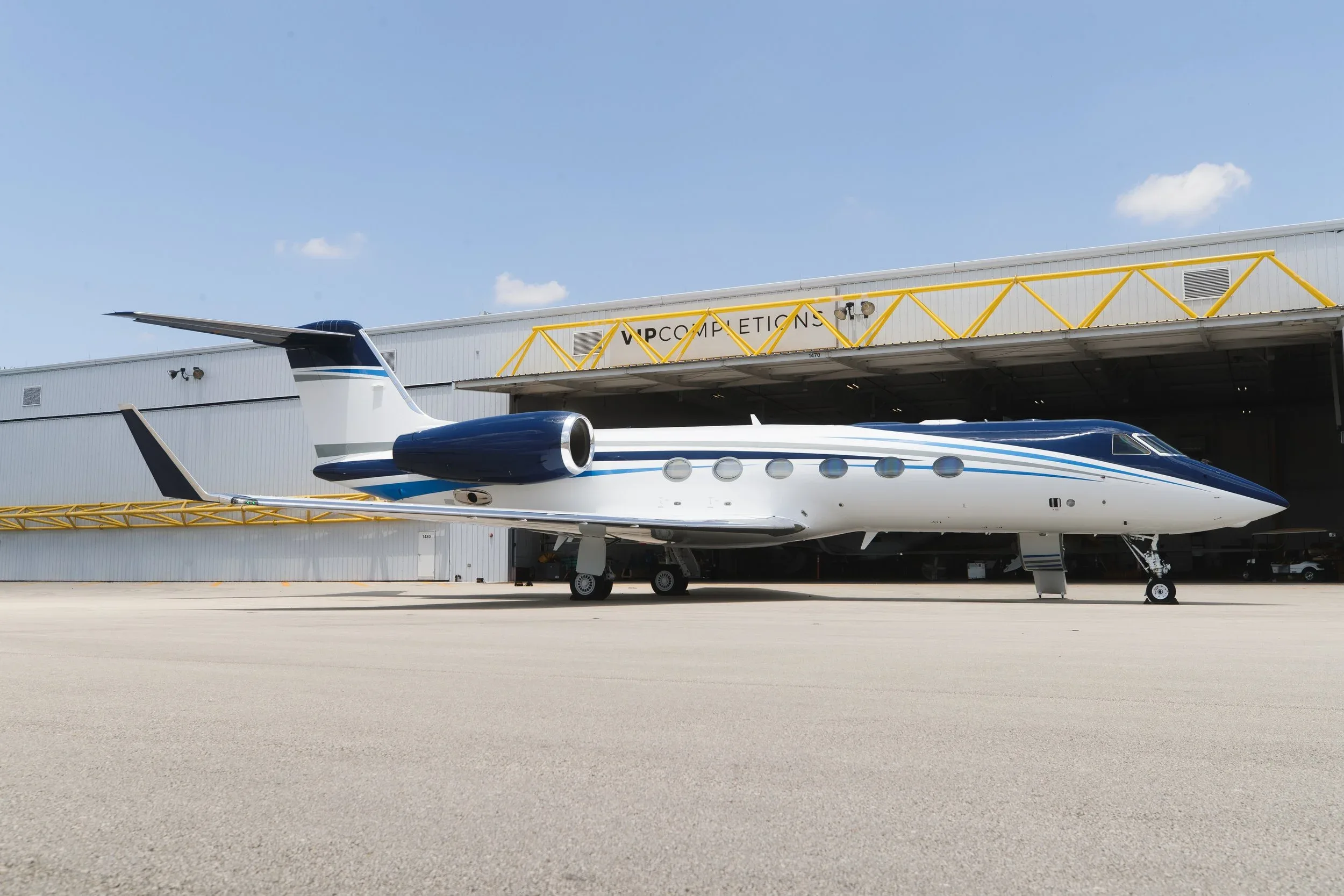 A white and blue Gulfstream business jet is parked on an tarmac in front of a hangar under a clear sky.