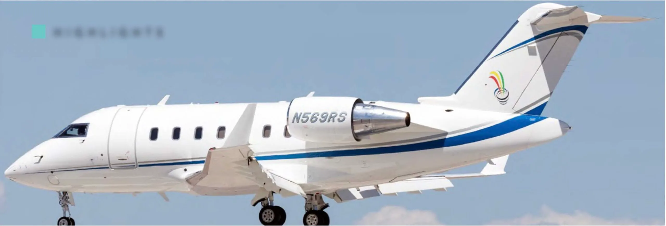 A white Bombardier Challenger business jet with blue and grey stripes and a tail logo, seen from the side against a blue sky.