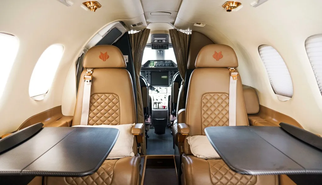 View from the aircraft cabin showing tan leather seats and a glimpse of the cockpit beyond.