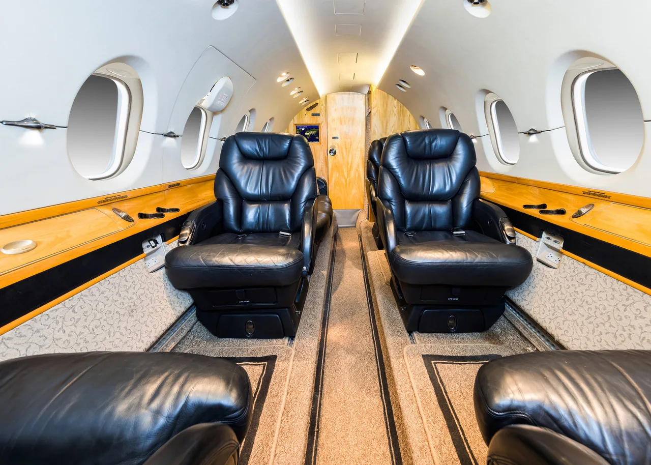 The luxurious interior cabin of a private jet with black leather seats and wood paneling.