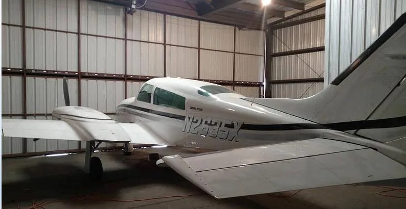 Rear-right view of a white twin-engine aircraft, N2635X, with black and gray stripes, inside a hangar.
