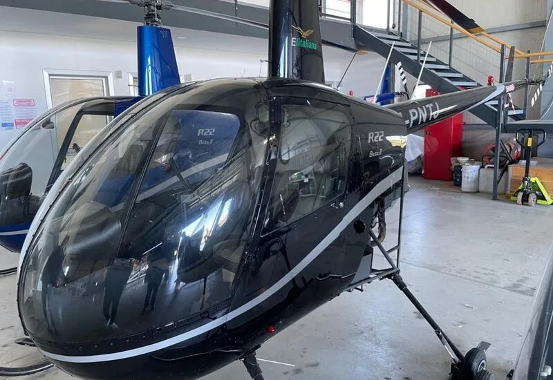 Close up of a black Robinson R22 Beta II helicopter with tail number I-PNTJ inside a hangar.