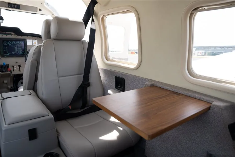 The light gray interior of an aircraft cabin featuring a fold-out wooden table and passenger seats.