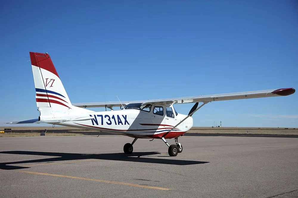 A white and red single-engine propeller aircraft, N731AX, parked on an airfield under a clear blue sky.