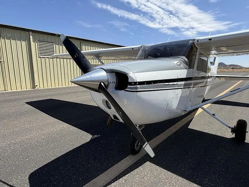 A close-up front-left view of the propeller and nose of the white Cessna 172, N738YW, on a tarmac.