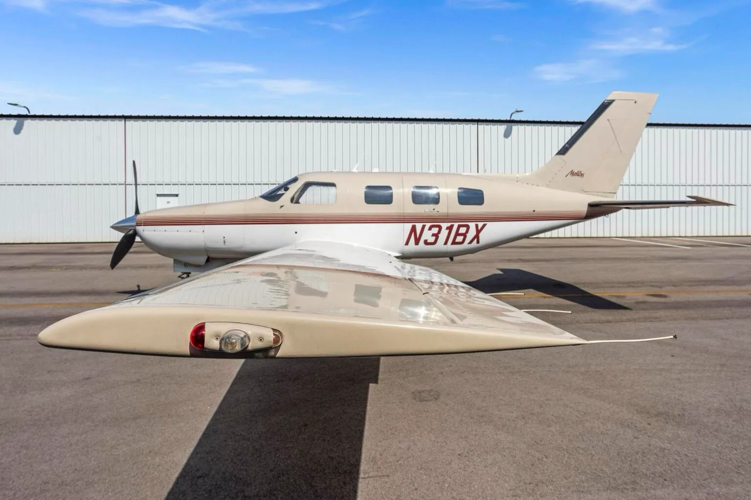 A close-up side view of the Piper Malibu N31BX showing the wingtip and landing gear on the tarmac.