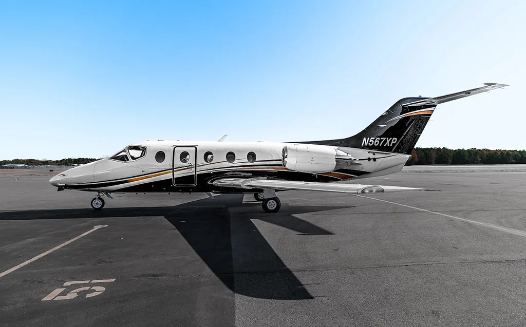 A white and black business jet with orange stripes and tail number N567XP is parked on an asphalt runway.