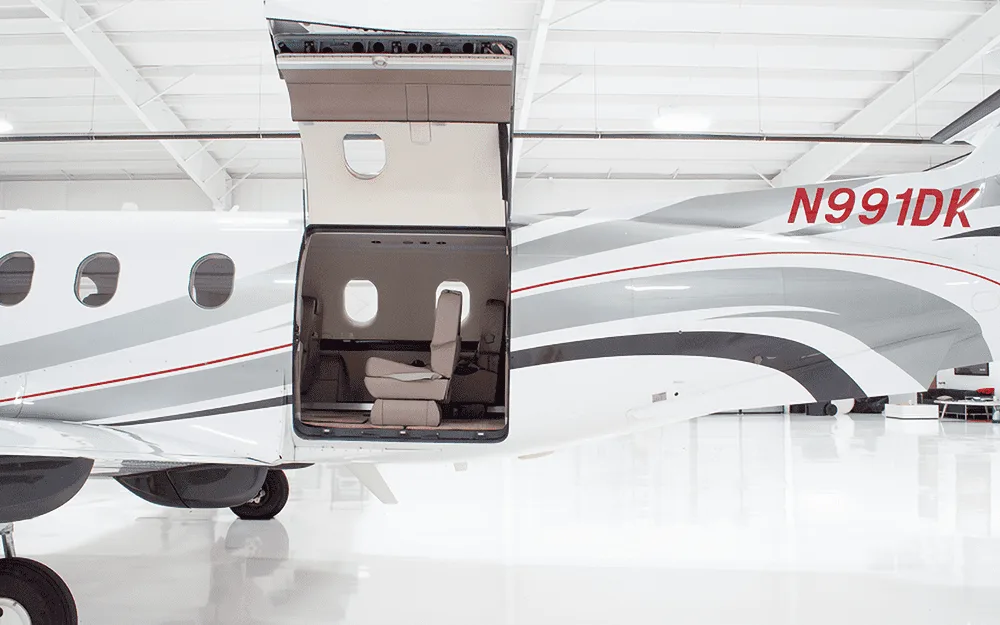 The rear fuselage of a white Pilatus PC-12 aircraft with its large cargo door open, showing a glimpse of the cabin.