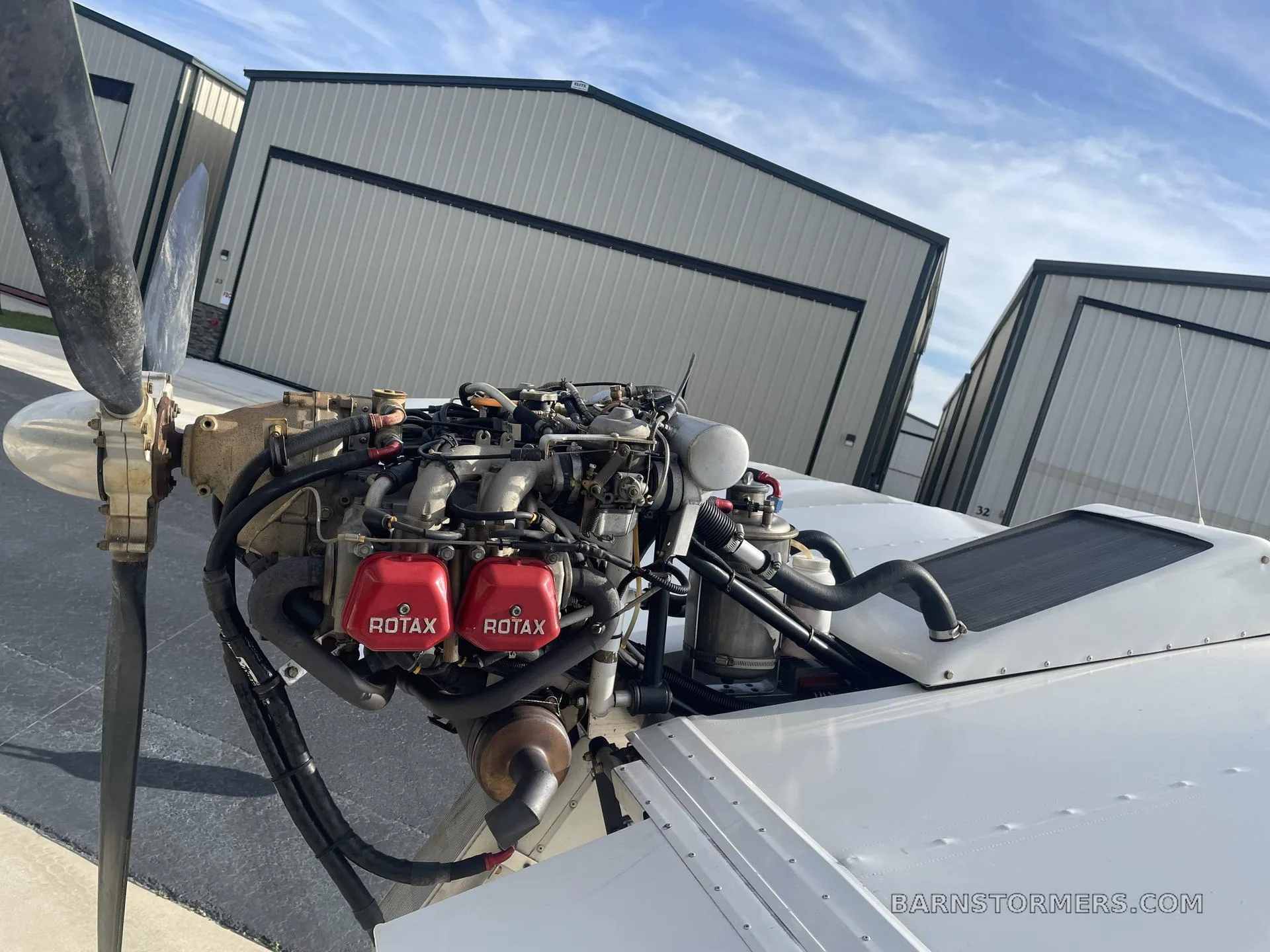 A close-up view of a Rotax aircraft engine and propeller, with hangars in the background.