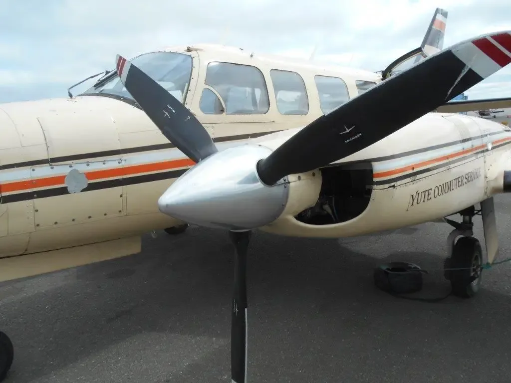 A close-up view of the front and right engine of the beige Piper Navajo aircraft, N4112E, showing the propeller and "Yute Commuter Service" text.