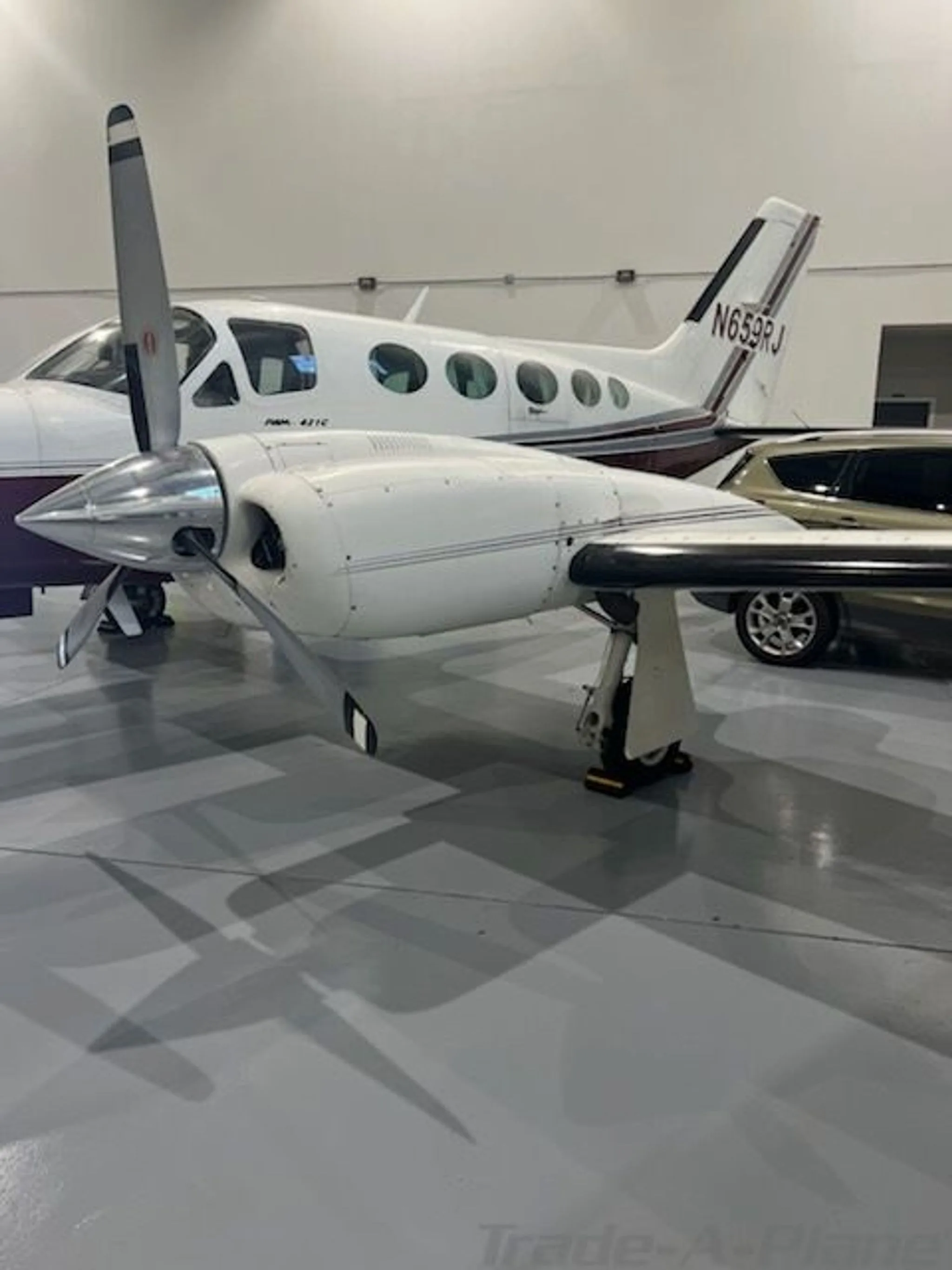 A close-up view of the right engine and propeller of a white and maroon Cessna 421C Golden Eagle aircraft (N659RJ) inside a hangar.