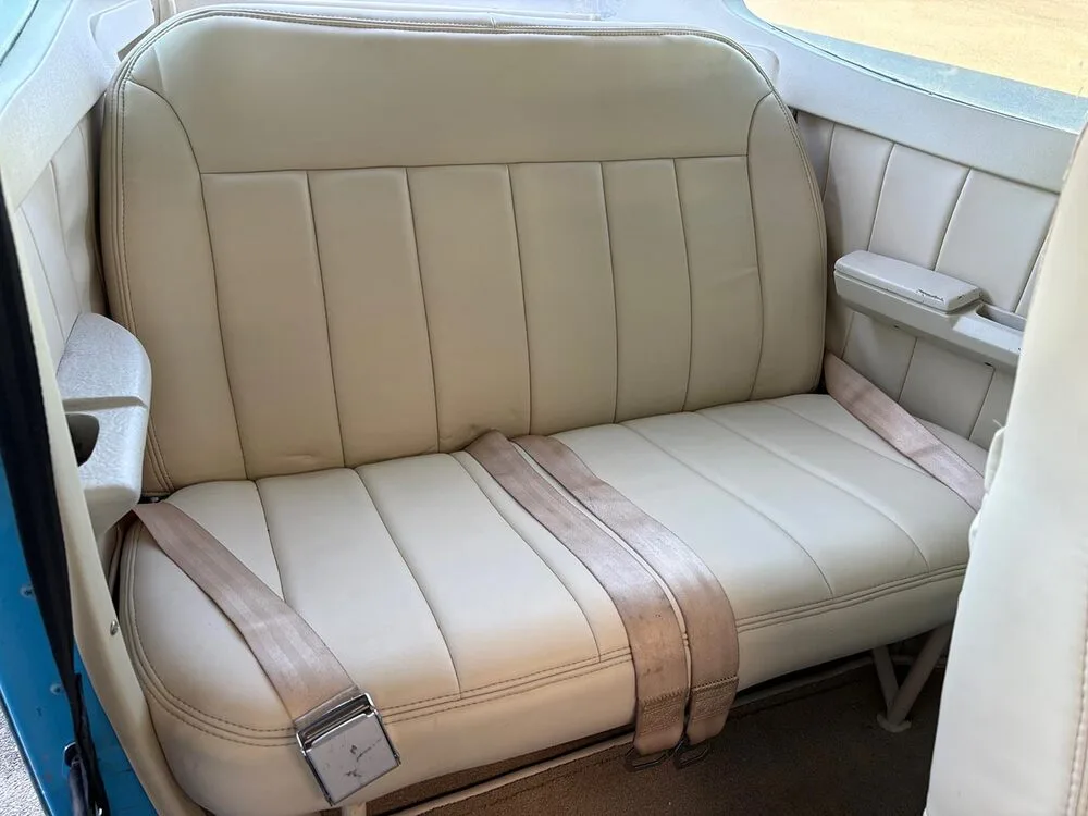The cream-colored rear passenger bench seat with seatbelts in the aircraft cabin.