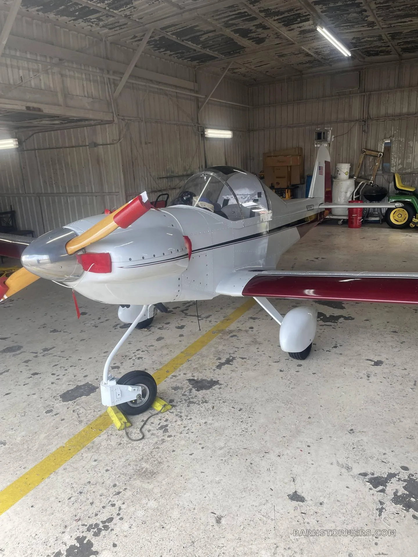 A white and maroon single-engine experimental aircraft with a tailwheel configuration, parked in a hangar.
