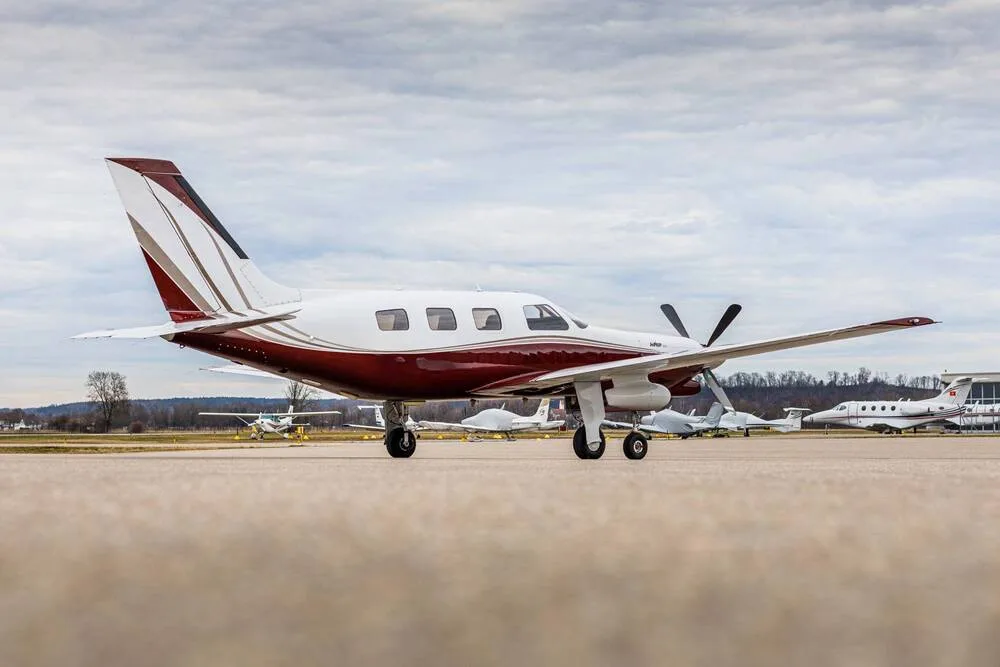A white and maroon single-engine turboprop aircraft parked on an airfield with other planes in the distance.