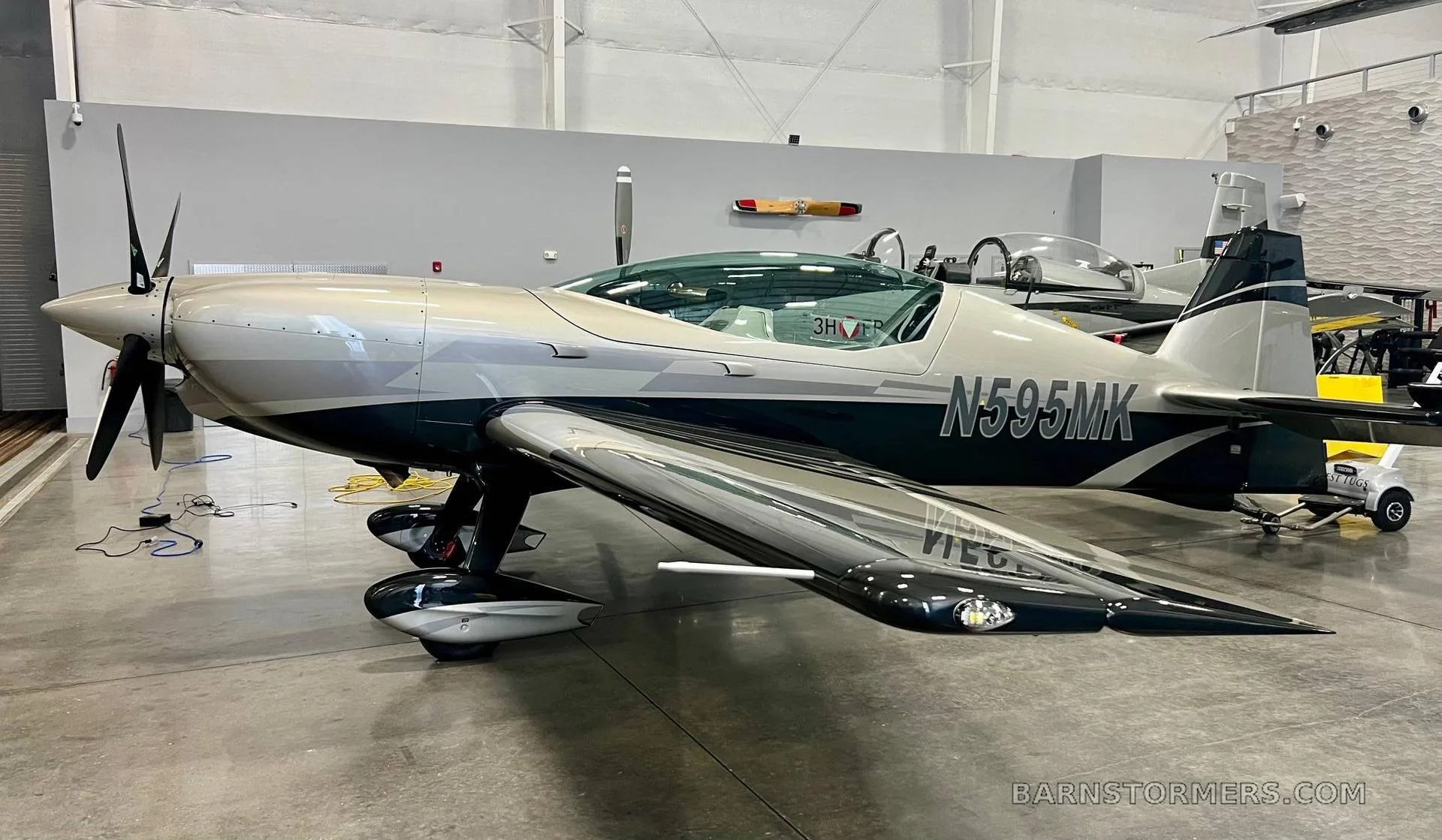 A two-tone silver and black propeller aircraft, registration N595MK, parked in a hangar.