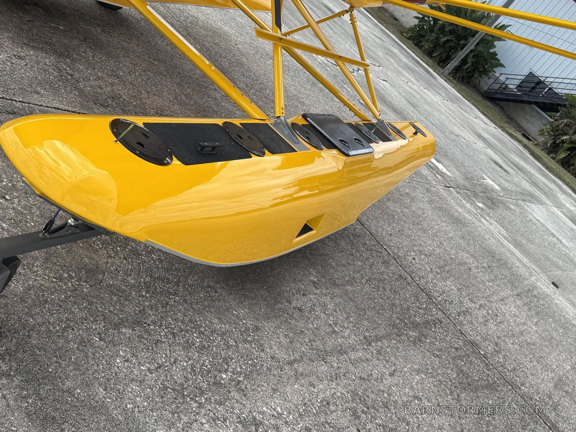 A close-up, low-angle view of the yellow float of an Air-Cam seaplane, showing access panels on top.
