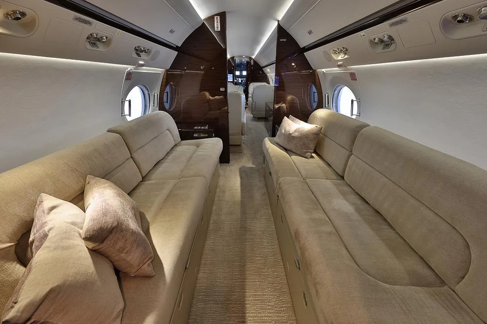 The aft section of a private jet cabin, featuring two long, comfortable beige couches with throw pillows.