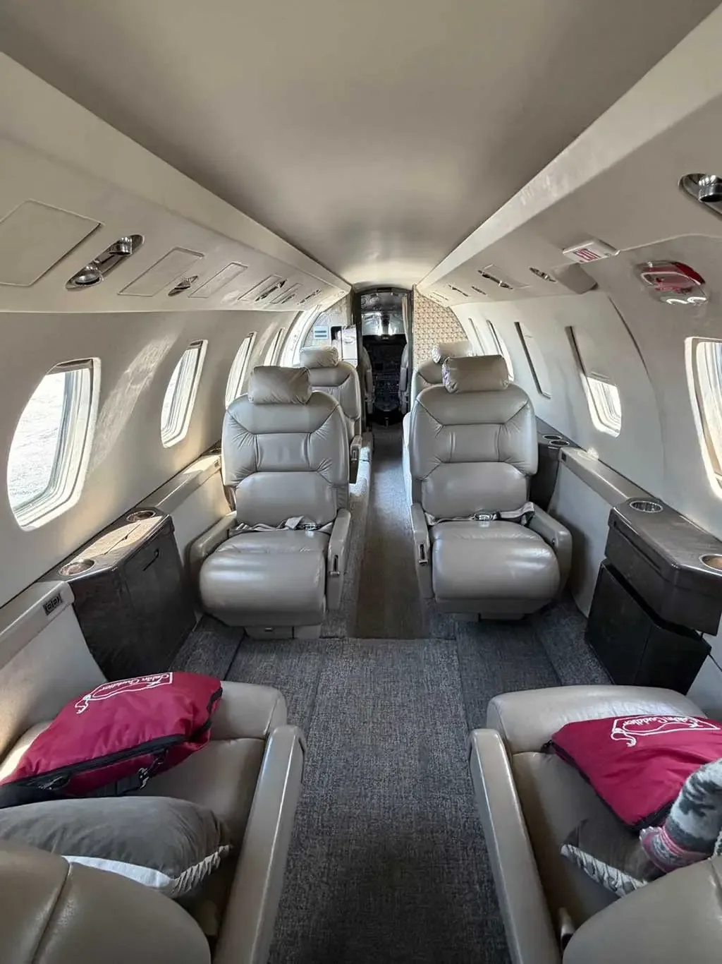 The interior cabin of a private jet, featuring beige leather seats arranged in a club configuration with a narrow aisle.