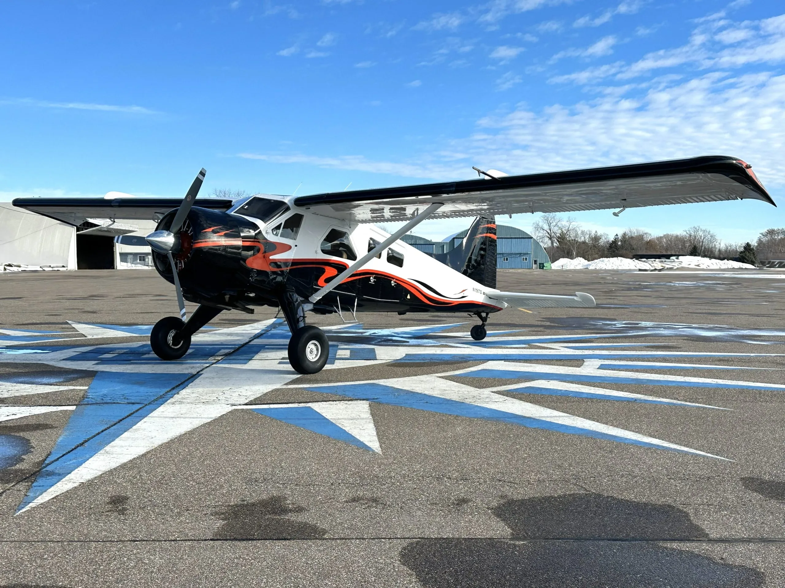 Full side view of a white and black single-engine turboprop aircraft with orange accents parked on an airfield.