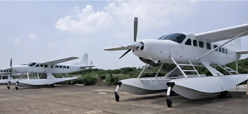 Several white floatplanes are parked on a concrete tarmac under a partly cloudy sky.