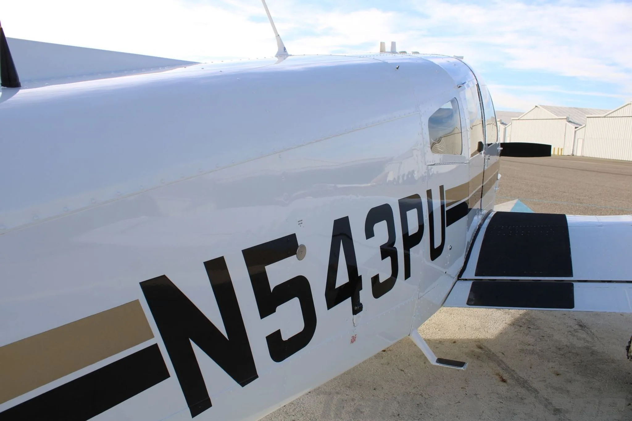 A close-up of the white fuselage of the N543PU Piper aircraft, showing black and gold stripes.
