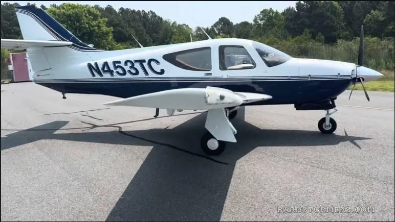 A white and blue single-engine aircraft, N453TC, is parked on an asphalt ramp with trees in the background.